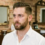 Homme aux cheveux fins avec une coupe courte texturée et une barbe de trois jours soignée dans un salon de barbier urbain