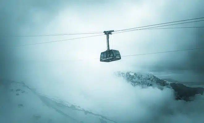 grey cable car traveling above snow covered mountain